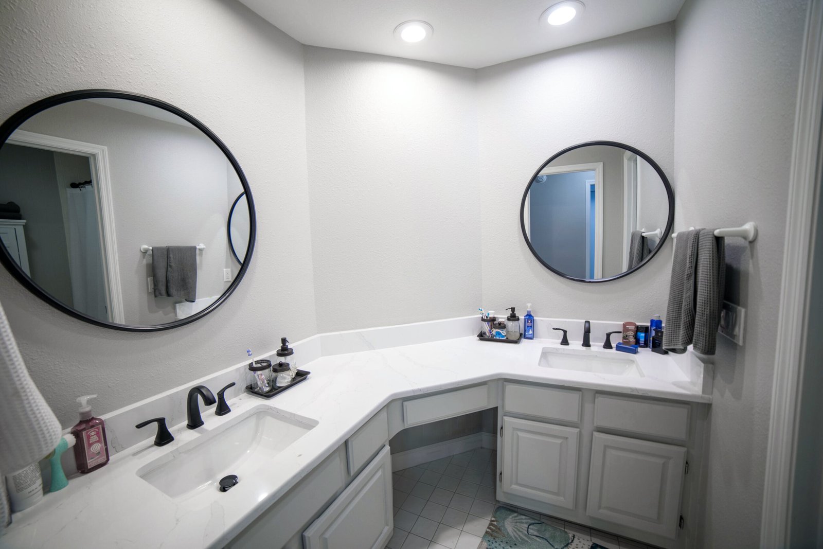 Corner bathroom vanity with light stone countertops, two sinks, and round mirrors